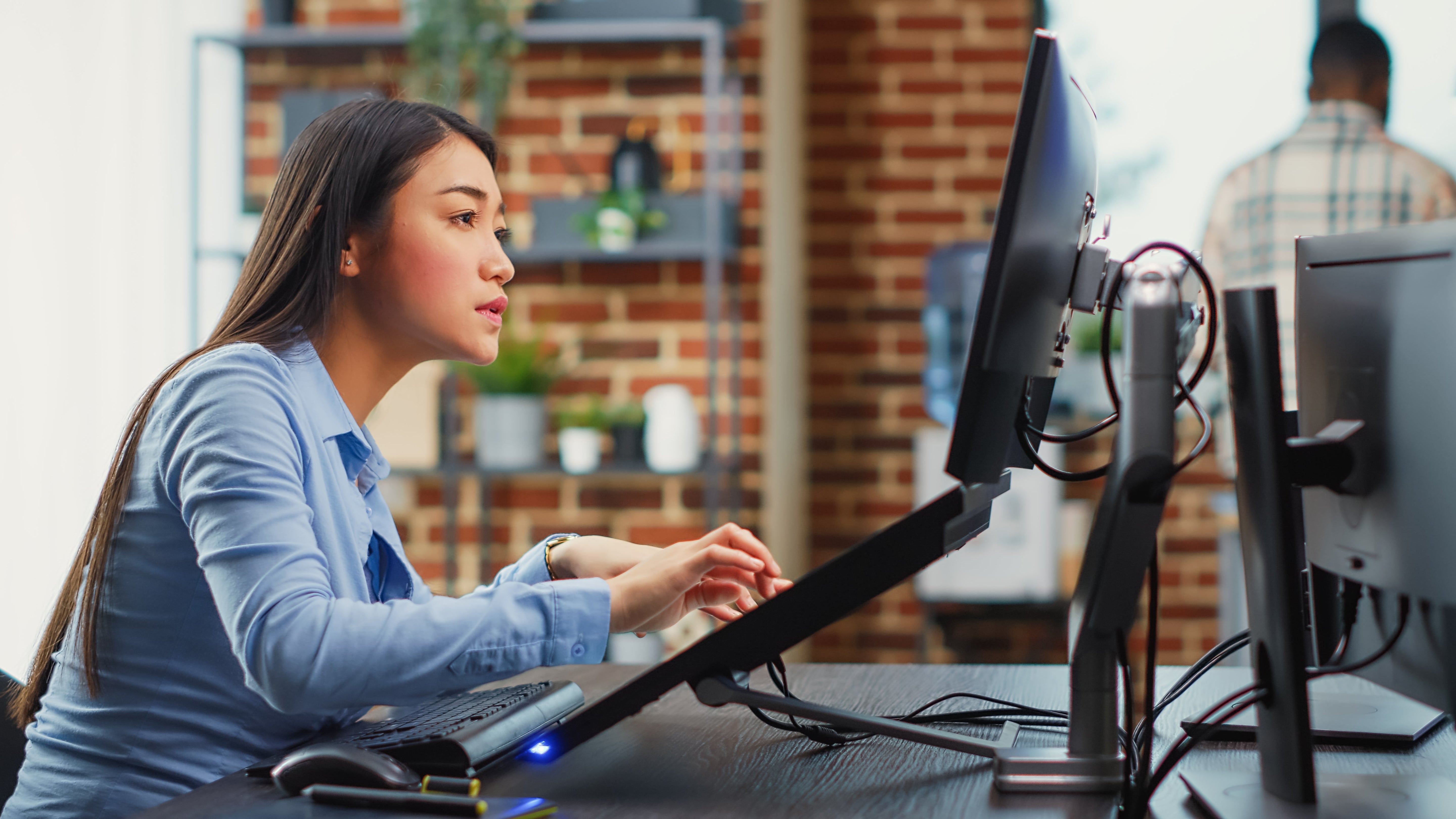 Professional using a VESA monitor arm with a dual monitor setup to achieve an ergonomic workstation for 24-, 27-, and 32-inch monitors.
