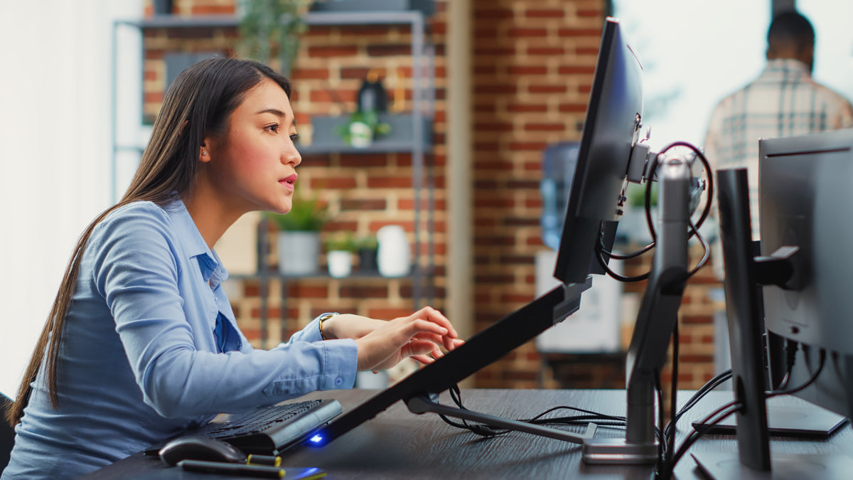 Professional using a VESA monitor arm with a dual monitor setup to achieve an ergonomic workstation for 24-, 27-, and 32-inch monitors.